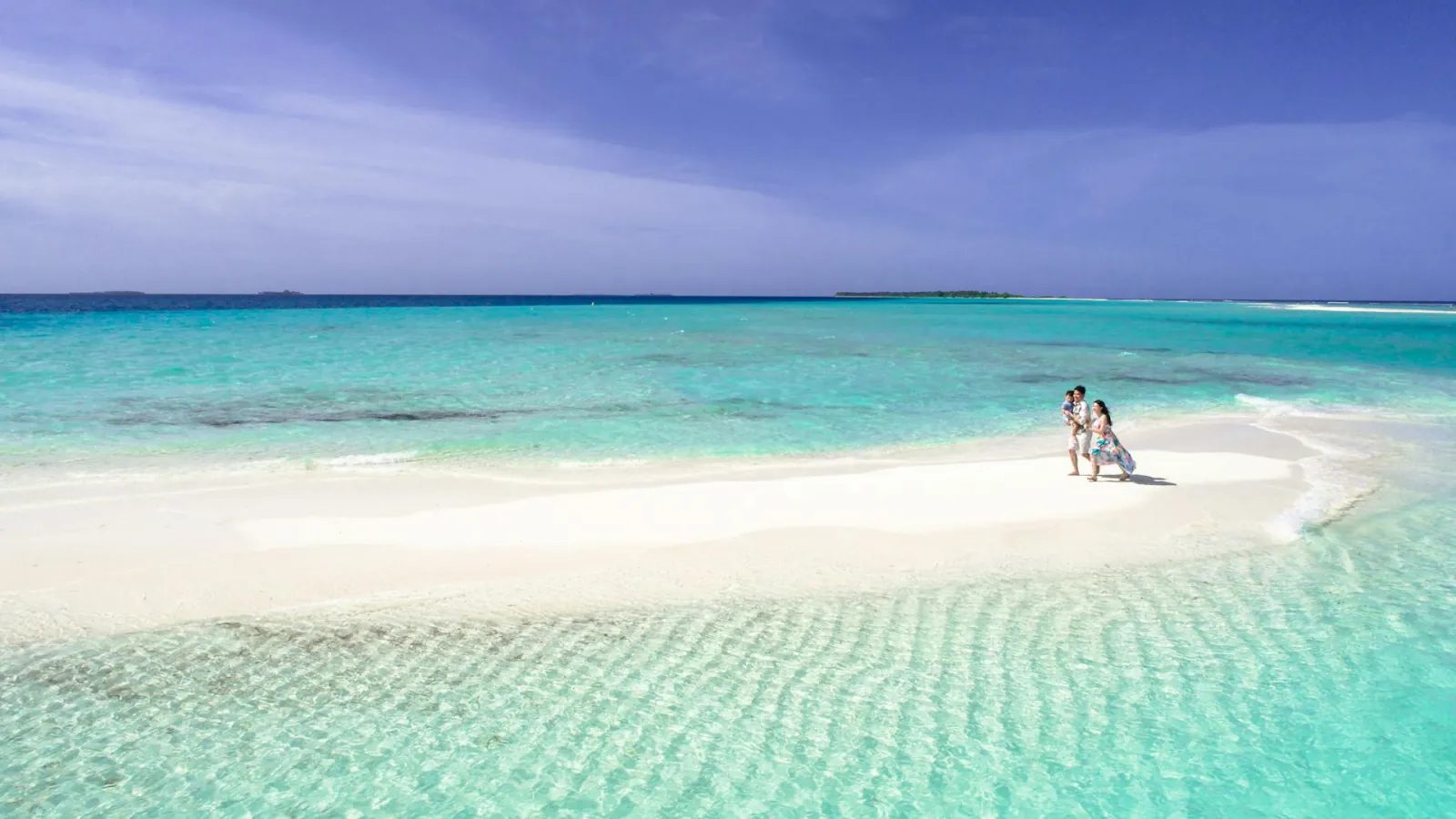 Two people on a sandbank in a turquoise lagoon