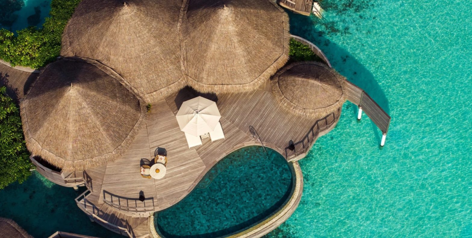 An Ocean House at The Nautilus, its thatched pavilions and private pool set over the lagoon, seen from above